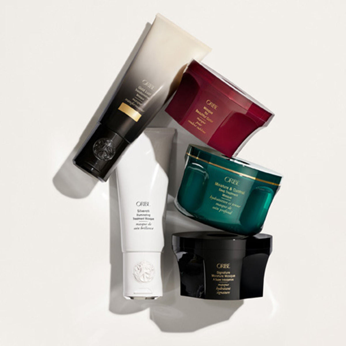 Three Signature Moisture Deep Conditioning Hair Masque jars in dark green, black, and maroon, and two tall reparative treatment tubes in white and pale beige, arranged in a pile.