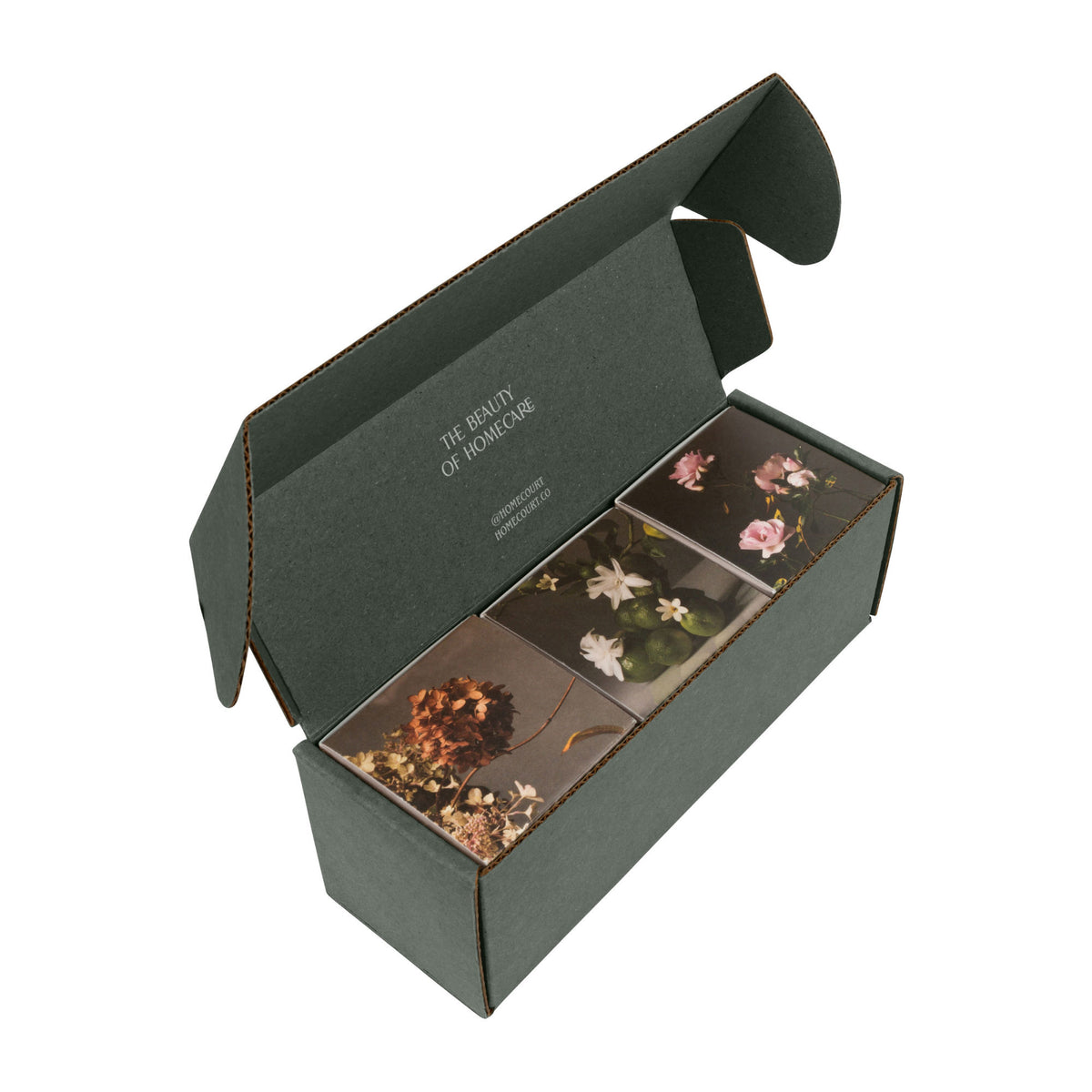 An open dark green cardboard Homecourt Candle Discovery Set (Limited Edition) containing three clean-burning home fragrance votives, each with a floral image on its top.