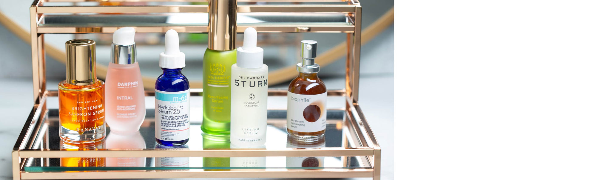 The products from the Serum Buying Guide on a gold and glass shelf