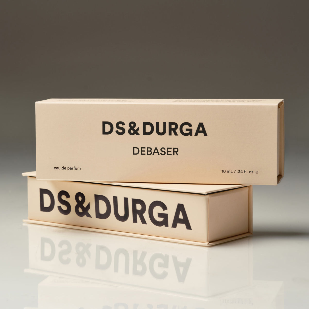 Two stacked, light tan rectangular D.S. & Durga Debaser Eau de Parfum boxes with the brand and product name in black text, sitting on a desk as indie rock plays over college radio.