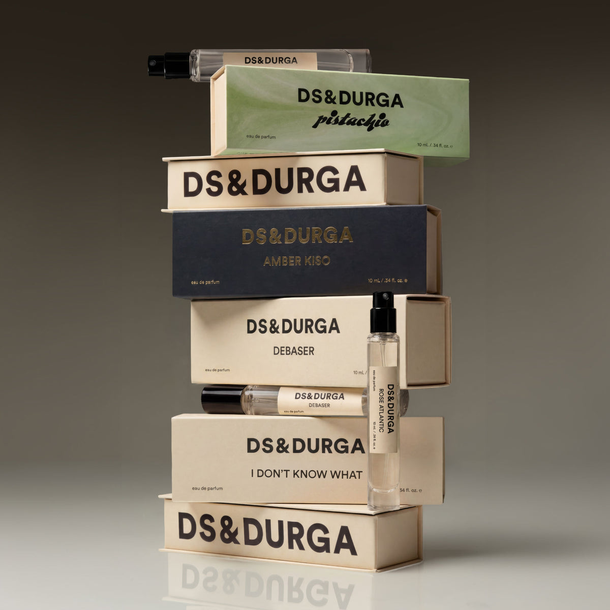 A vertical stack of Debaser Eau de Parfum rectangular boxes and two glass spray vials, reminiscent of an indie rock aesthetic in the August heat.
