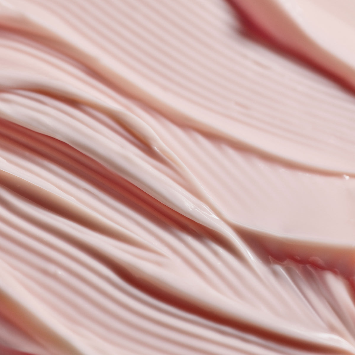 A close-up texture shot of Joie The Emulsion pale pink radiance cream, featuring smooth, distinct ridges.