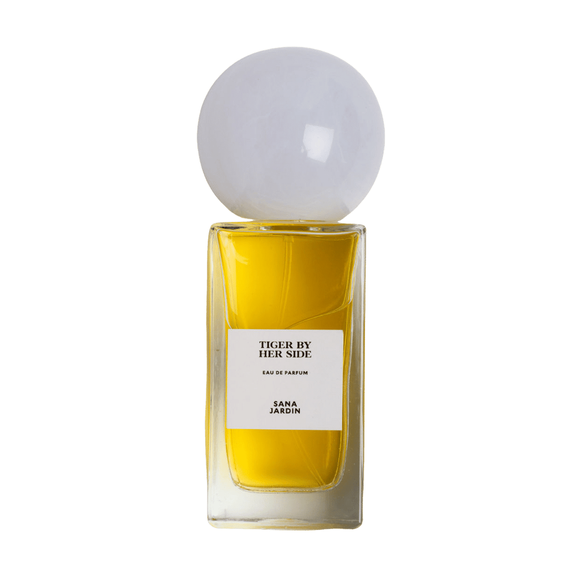 A rectangular amber-colored bottle of Tiger By Her Side Eau de Parfum by Sana Jardin, featuring a large, spherical white cap and notes of patchouli.