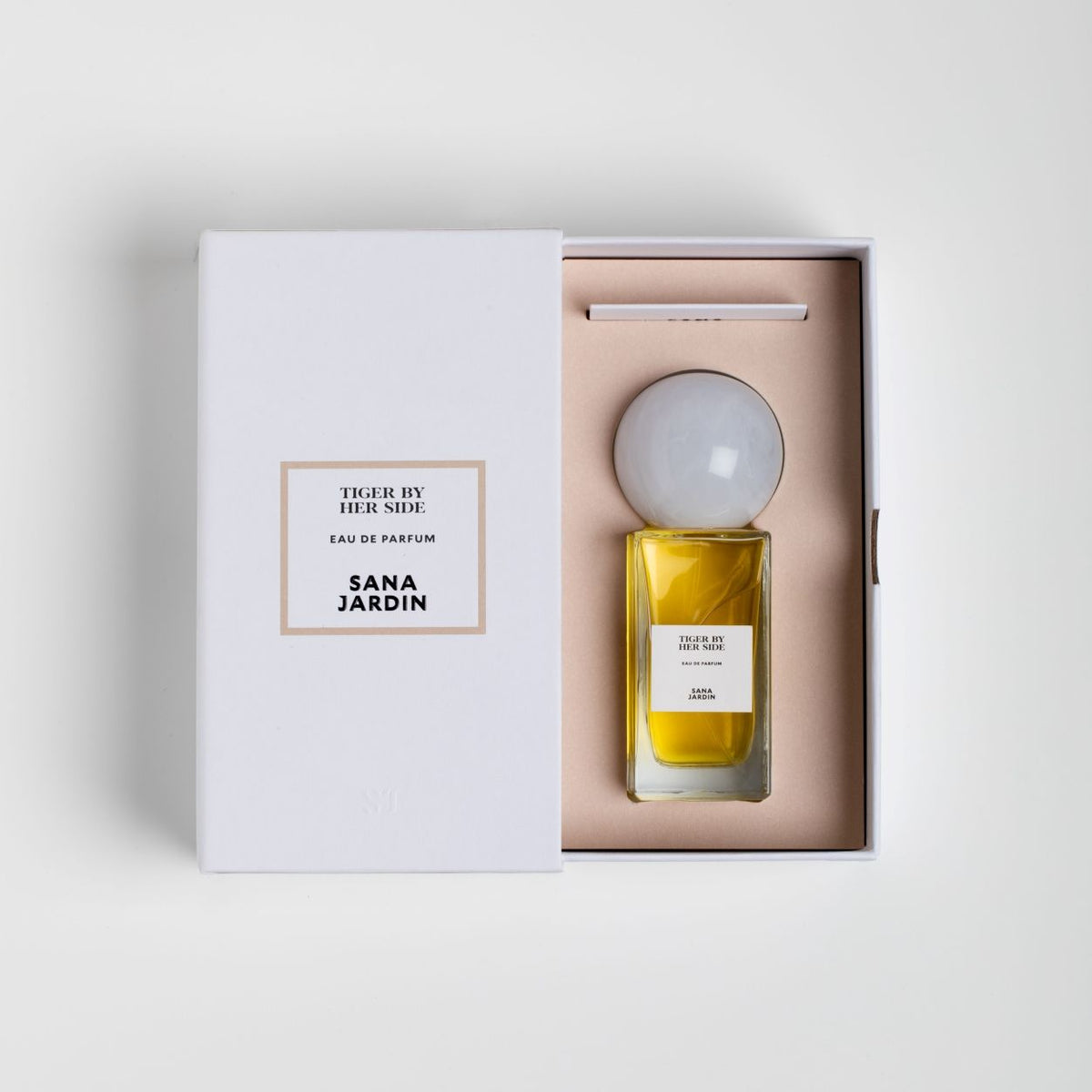 Tiger By Her Side Eau de Parfum in a white presentation box, featuring a perfume bottle with a large, round white cap, golden amber liquid, and matching branding on the box lid and bottle label.