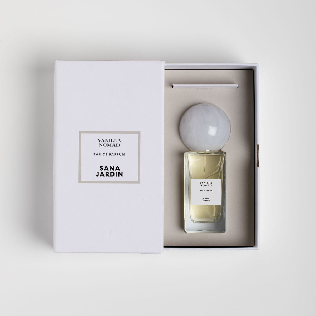 Vanilla Nomad Eau de Parfum in a rectangular bottle with a round marbled cap, resting inside an open white presentation box with matching labels.