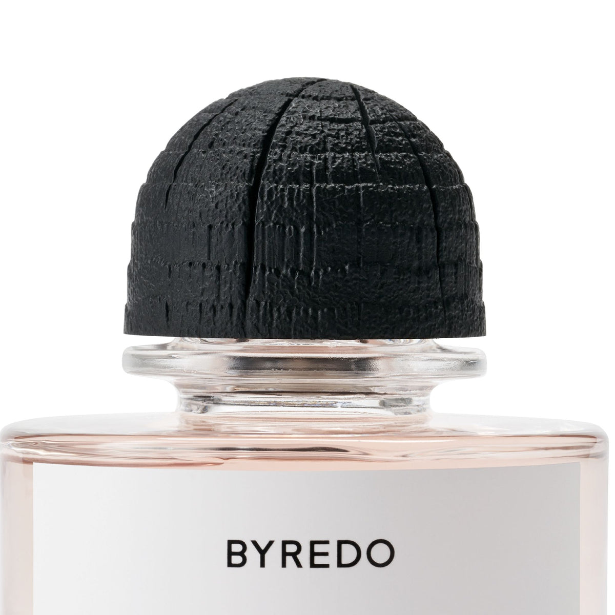 A glass bottle of Byredo Rose of No Man’s Land Absolu de Parfum filled with pink liquid and topped with a textured black rounded cap.