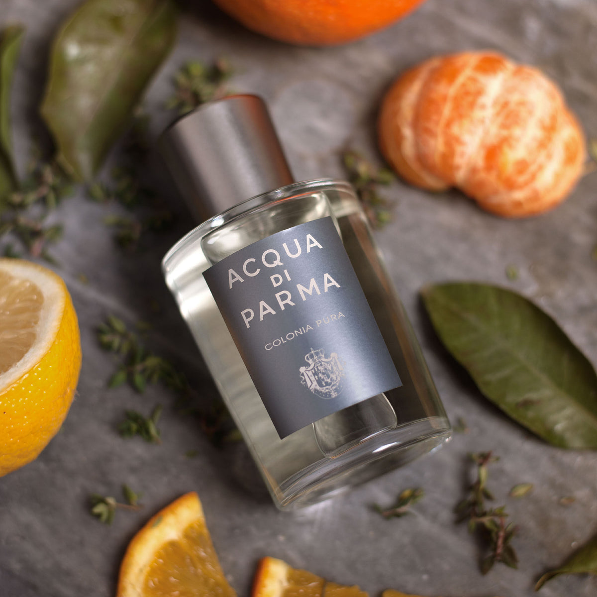 A bottle of Acqua di Parma Colonia Pura Eau de Cologne surrounded by slices of orange and lemon on a stone surface.