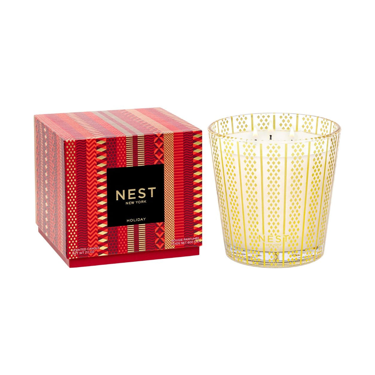 A Nest New York Holiday Candle (Limited Edition) in a three-wick, gold-patterned glass jar sits next to its red box featuring a decorative geometric stripe pattern.