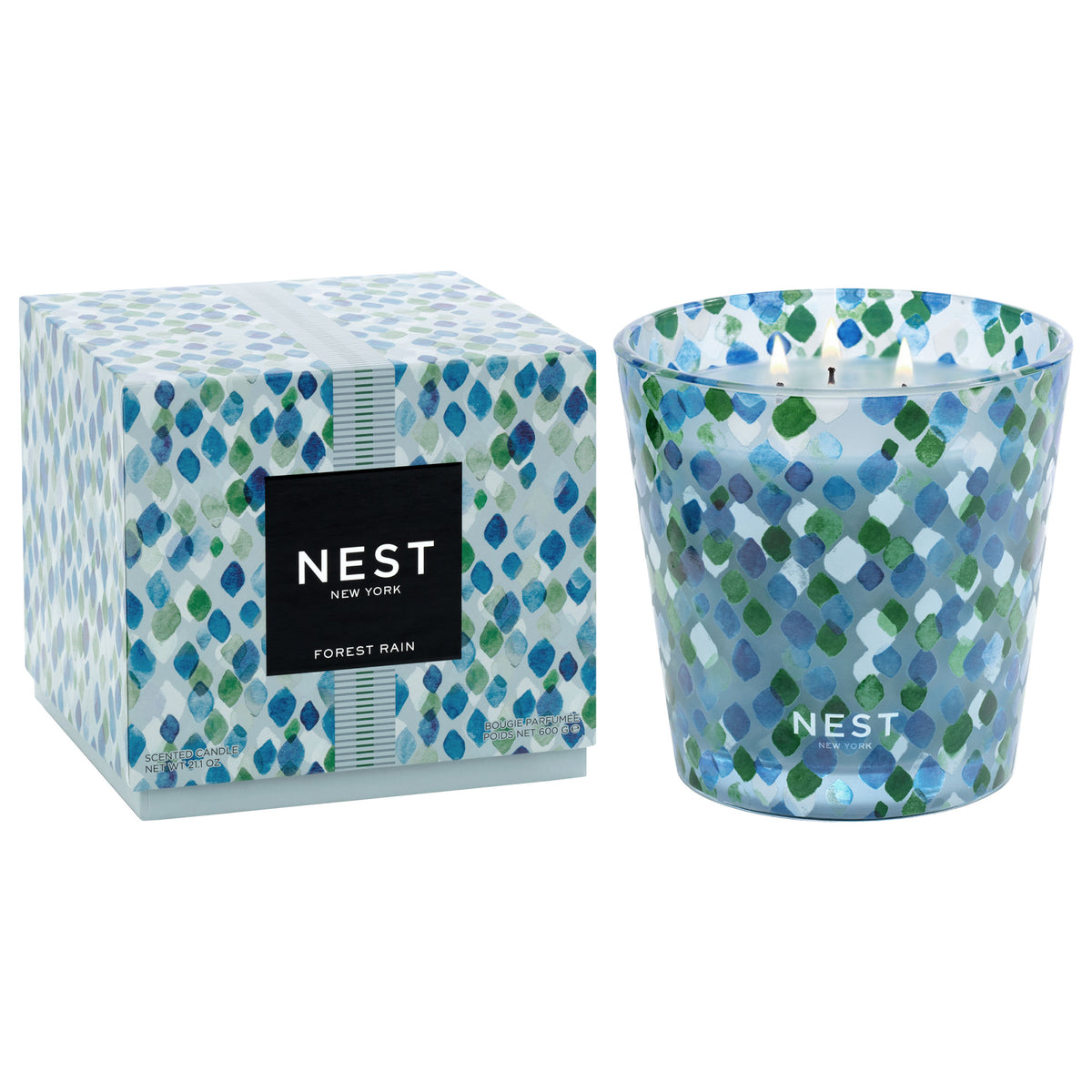 A Nest New York Forest Rain three-wick scented candle in a glass vessel and its matching square box, both featuring a blue and green painted diamond pattern evocative of dewy fig leaves.
