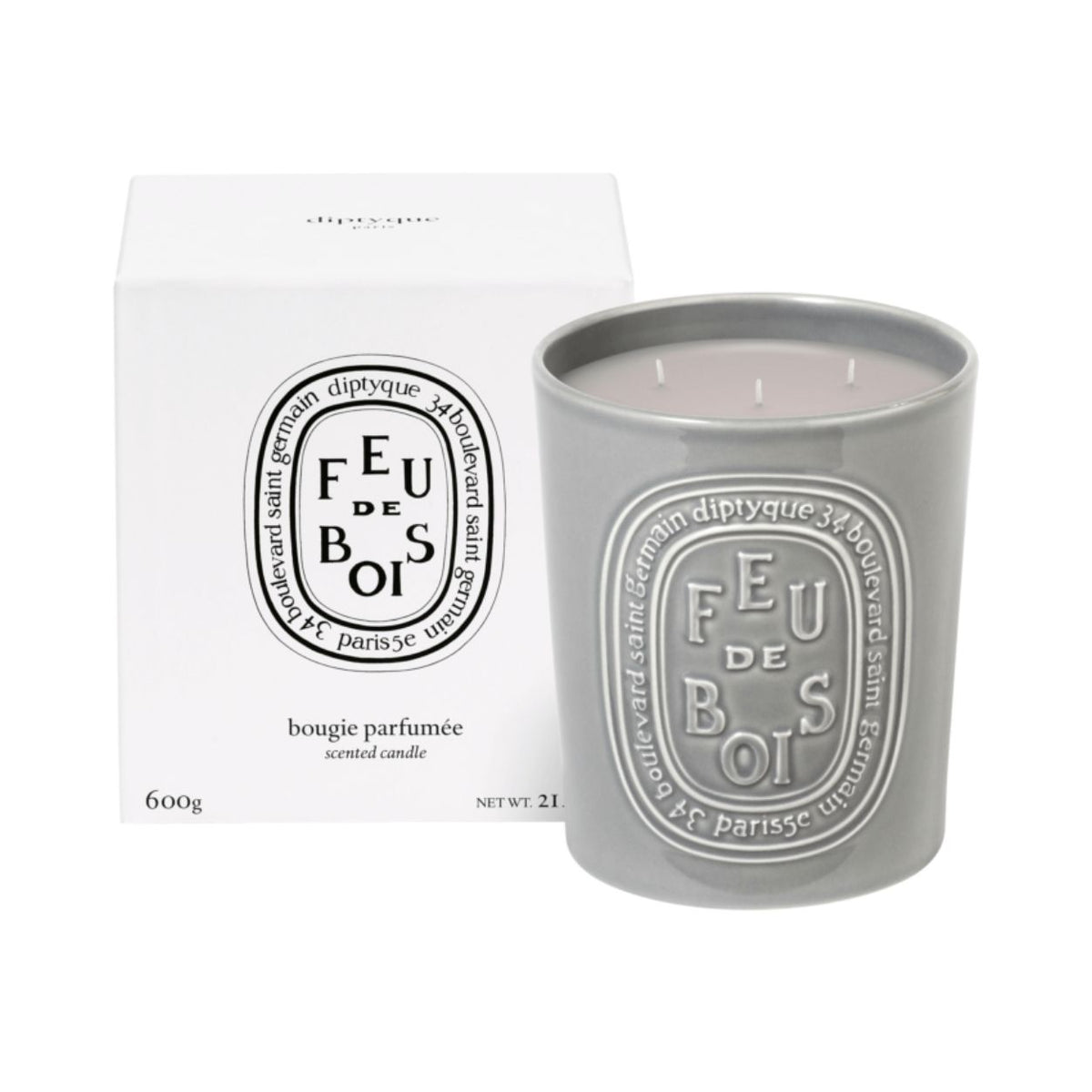 A grey three-wick Diptyque Feu de Bois candle in an embossed ceramic vessel next to its white cardboard box, perfect for a winter fireplace.