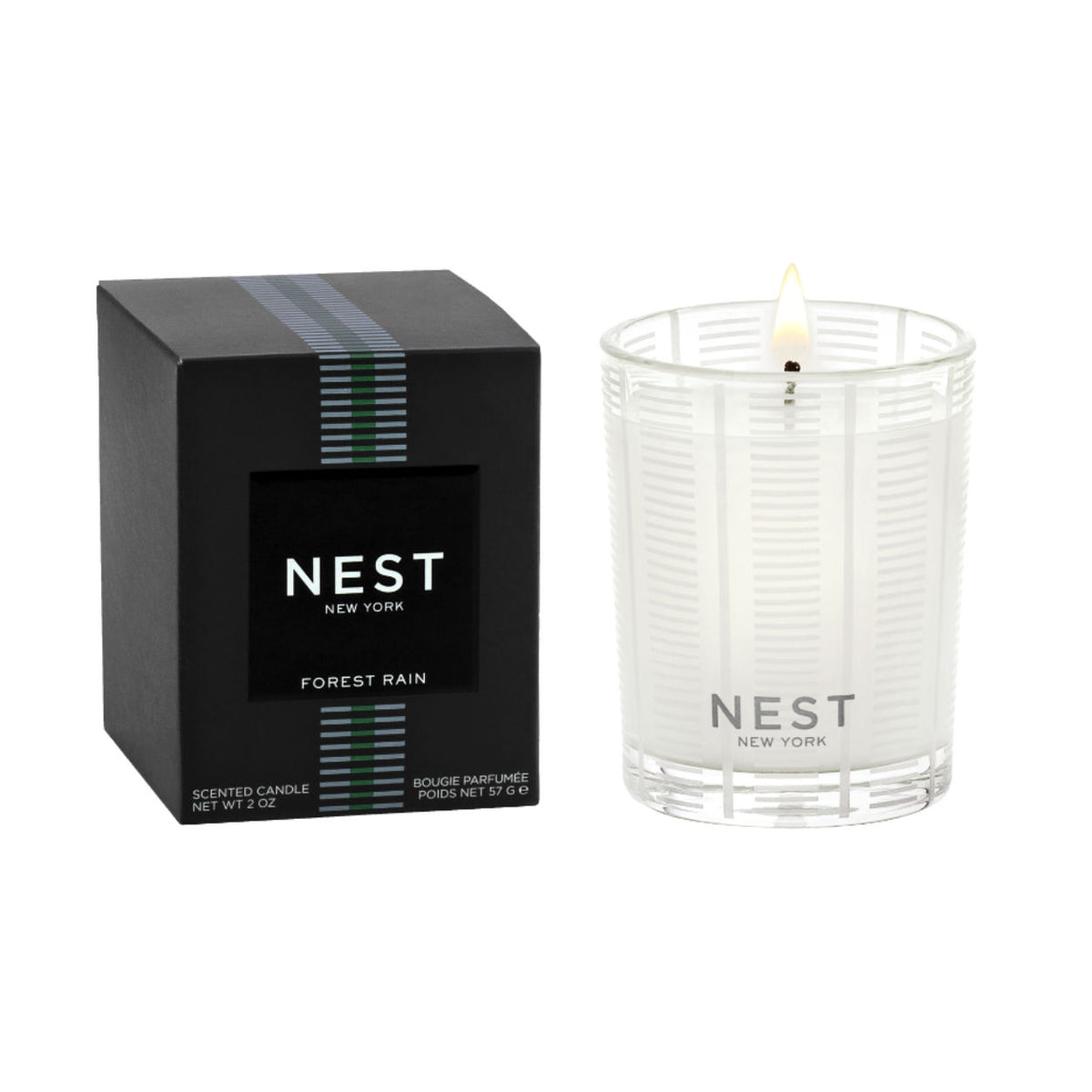A Nest New York Forest Rain candle in a white waterlily-patterned glass next to its black box.