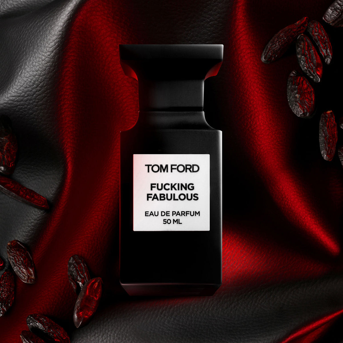 A black Tom Ford F’ing Fabulous Eau de Parfum Spray bottle with a white label, surrounded by scattered dark seeds for an intoxicating scent.