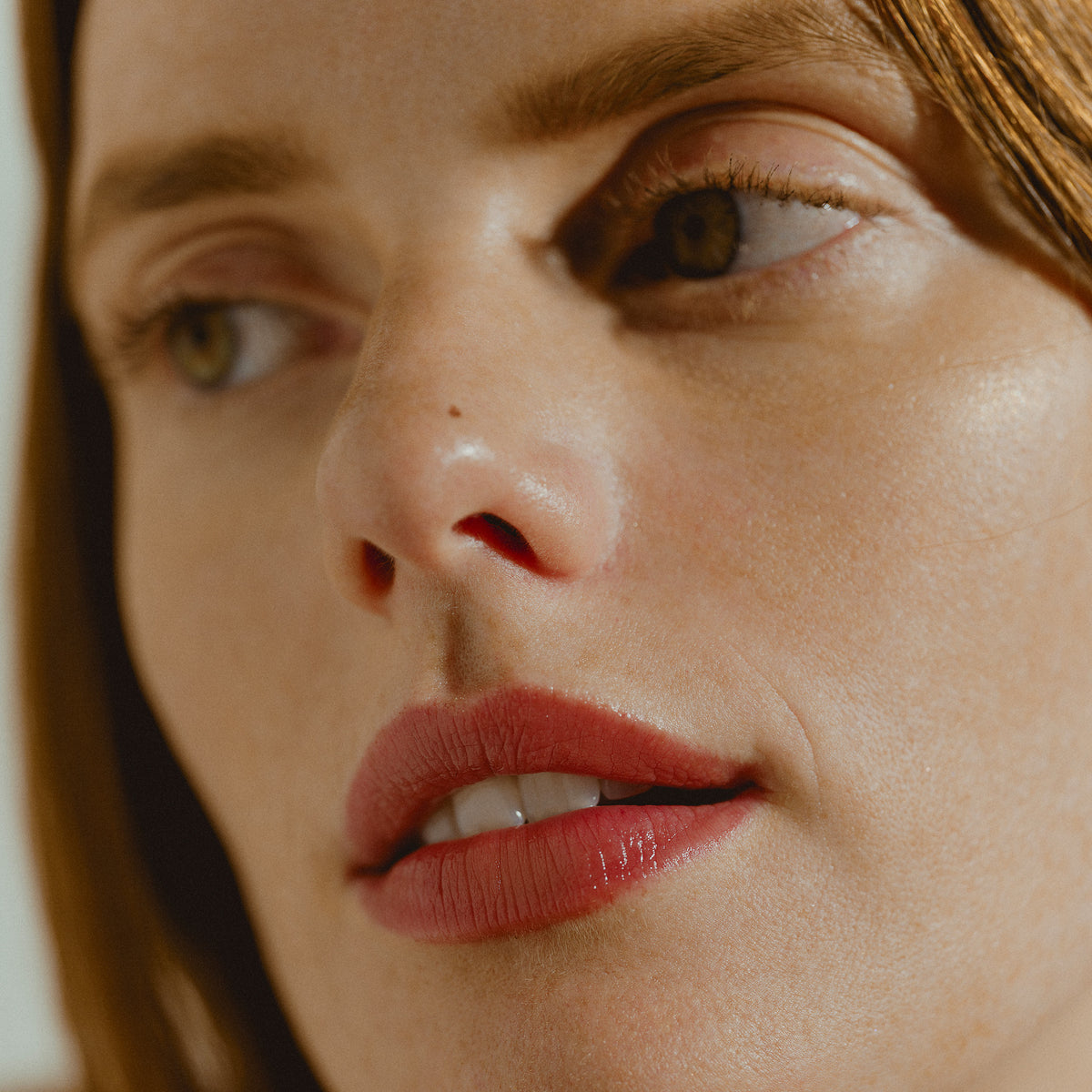 Close-up of a woman’s face, highlighting her intense, rose-colored lips wearing Sisley Paris Phyto-Rouge Shine with a balm-like sensation.