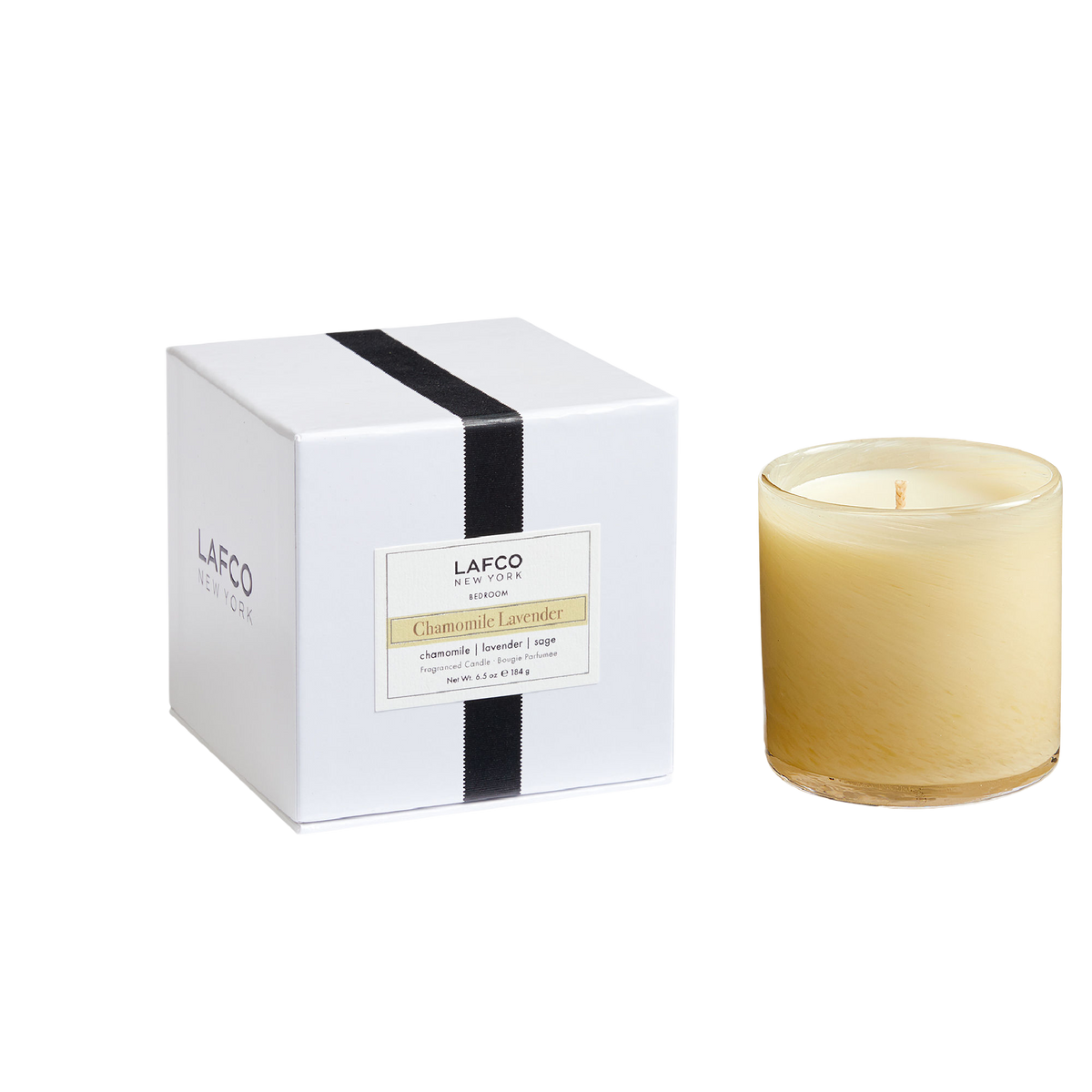 A white Chamomile Lavender Candle box with a black ribbon and a gold-toned label, next to a matching glass-vessel candle.
