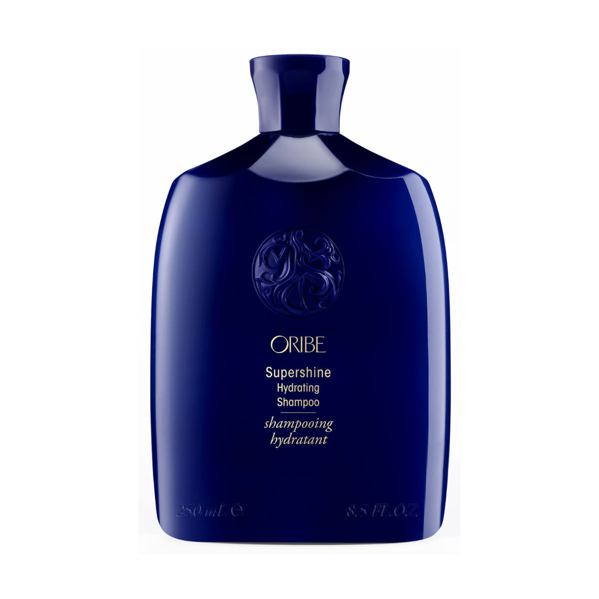 Dark blue bottle of Oribe Supershine Hydrating Shampoo for Dry Hair with an embossed emblem on the front and white text listing product details, lasting luster, and volume.