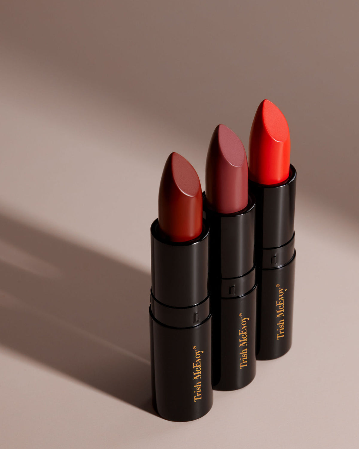 Three Trish McEvoy Easy Lip Color tubes in beautiful hues of red and berry, standing upright.