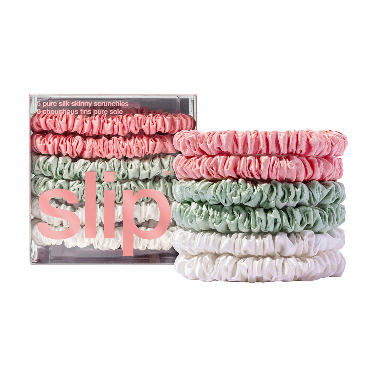 A clear box of six Slip Pure Silk Skinny Scrunchies in pink, green, and white, with three additional scrunchies of the same colors stacked next to it.