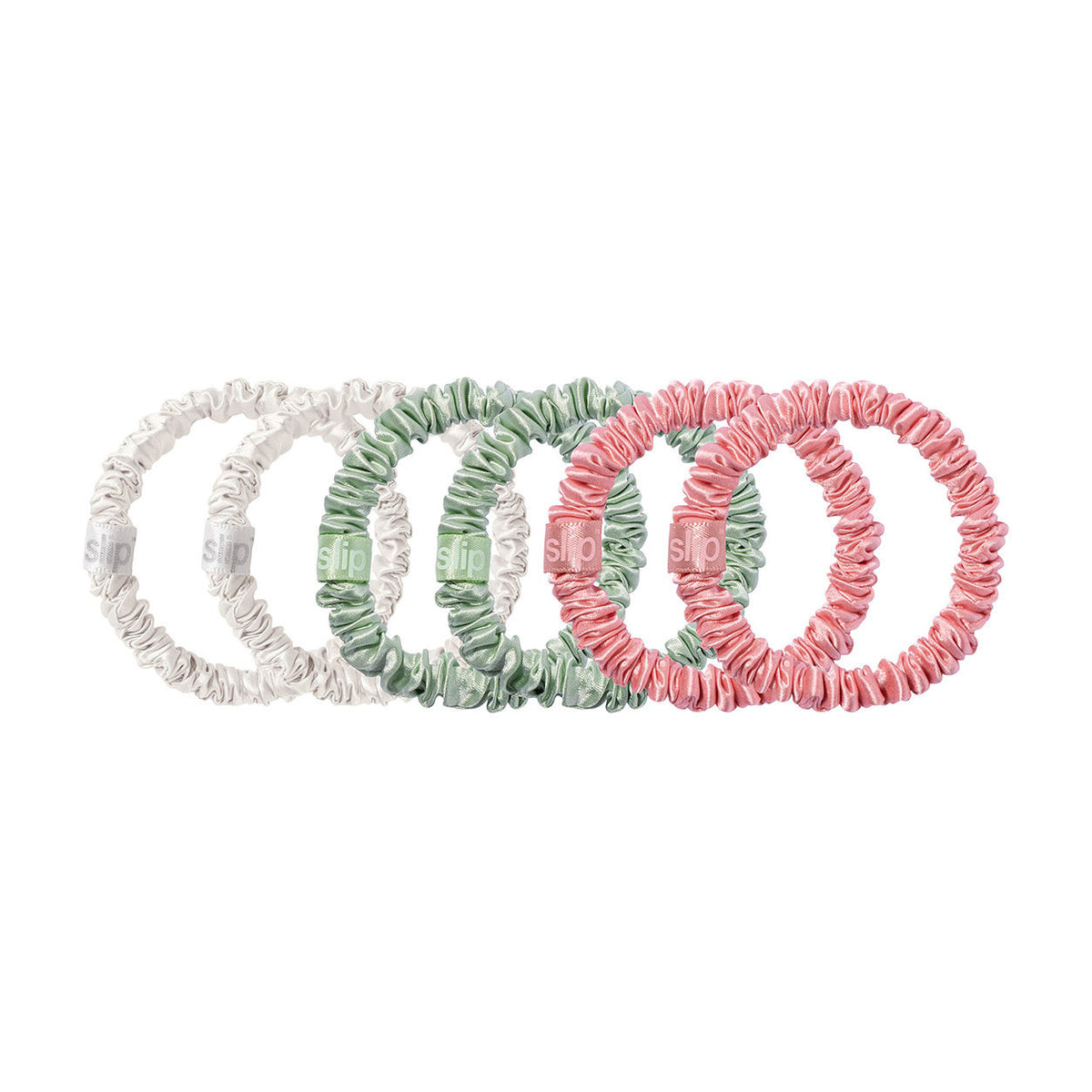 Six Slip Pure Silk Skinny Scrunchies in white, sage green, and pink arranged in a row to prevent hair creases.