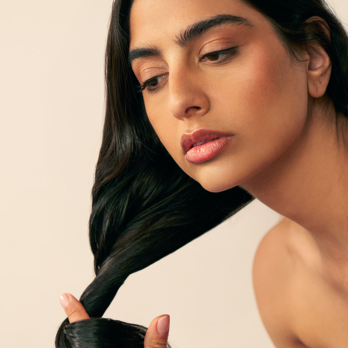 A person with dark, medium to thick hair looks down while applying Christophe Robin Night Recovery Monoï Oil with White Lotus Flower to a section of their hair.