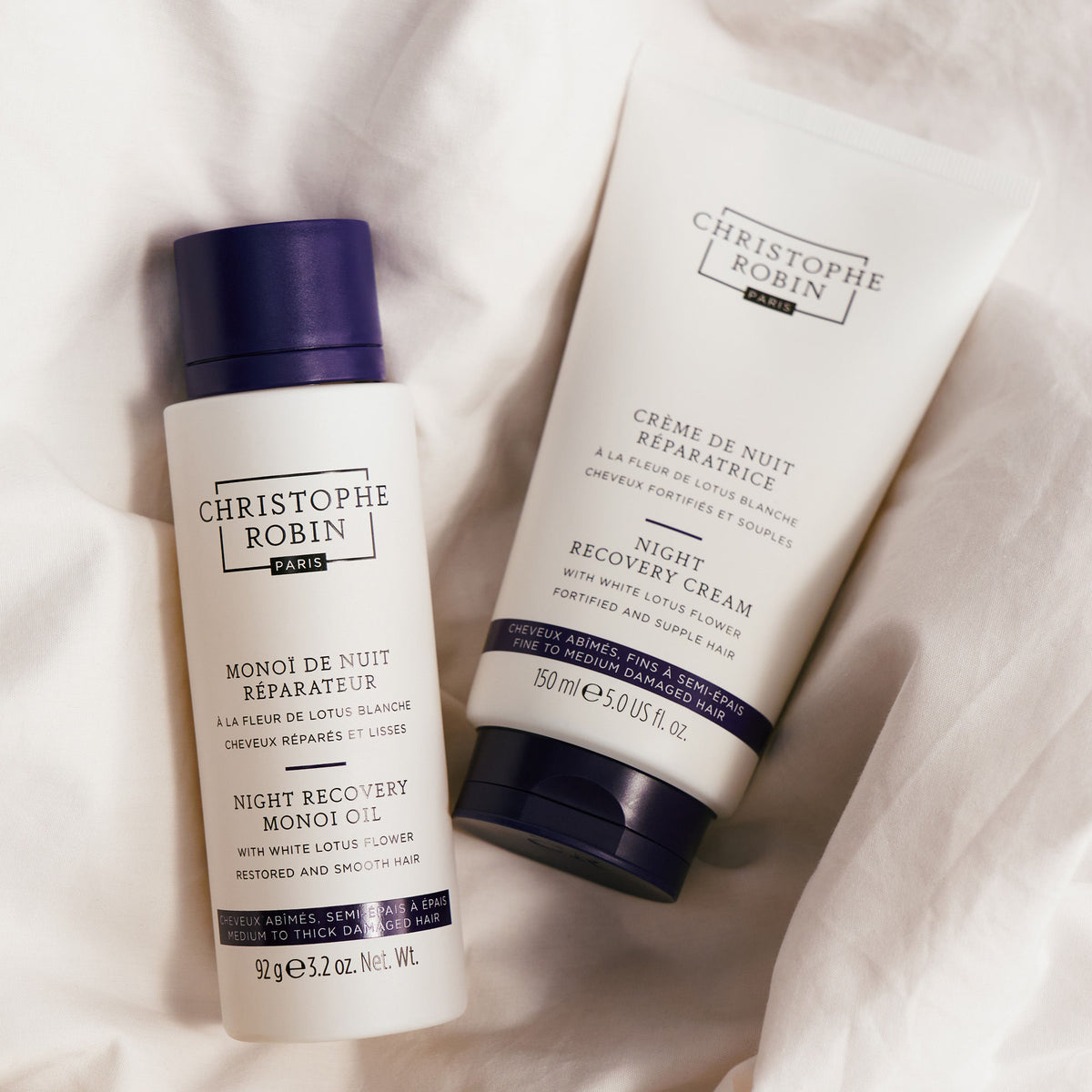 A bottle of Night Recovery Monoï Oil with White Lotus Flower and a tube of night recovery cream resting on white fabric to strengthen and protect hair.