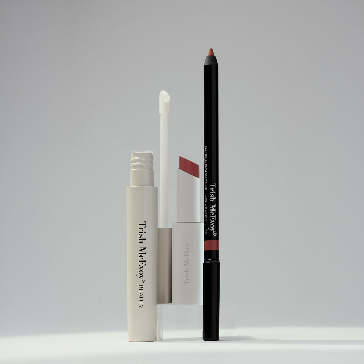 Trish McEvoy The Bluemercury Exclusive Plump, Protect & Perfect Nude Lip Wardrobe (Limited Edition) featuring a lip gloss with an applicator wand, a nude lipstick, and a brown lip liner pencil displayed upright for a perfected, fuller look.