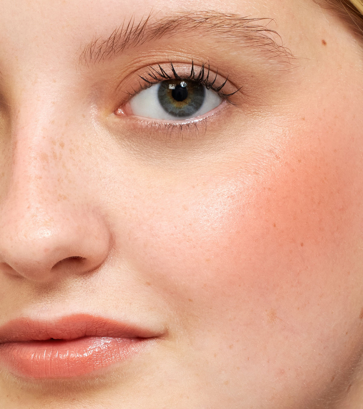 Close-up of a face wearing peach-toned Going Rouge Cream Cheek and Lip on the cheeks and lips.