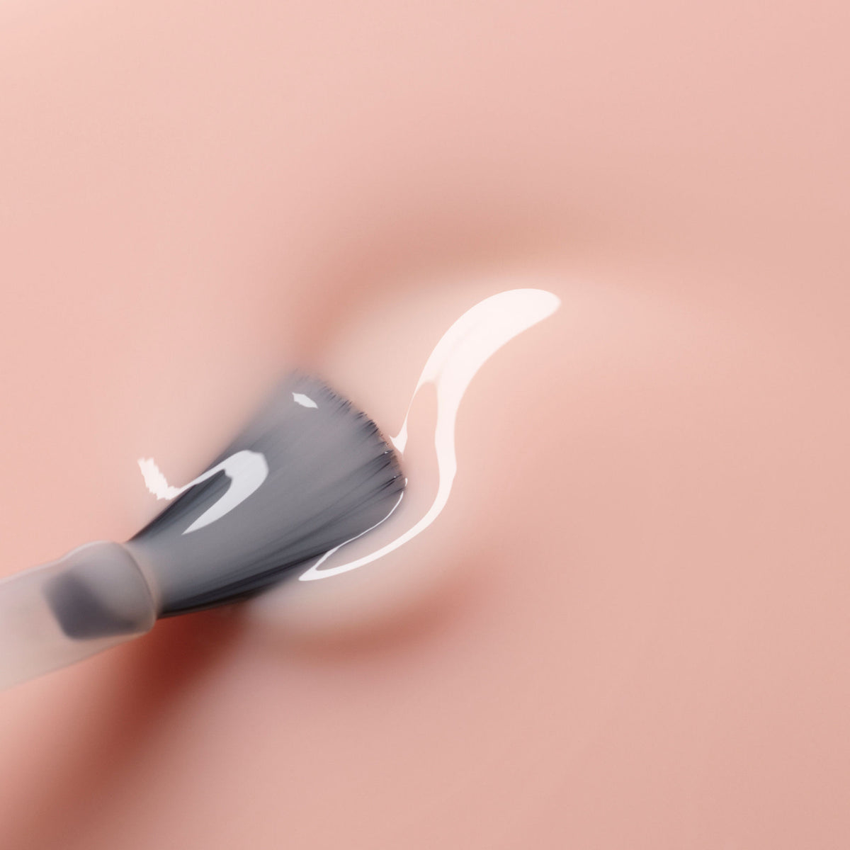 A Poppy Red nail polish brush strokes a drop of non-toxic, clear liquid onto a smooth, pale pink surface.