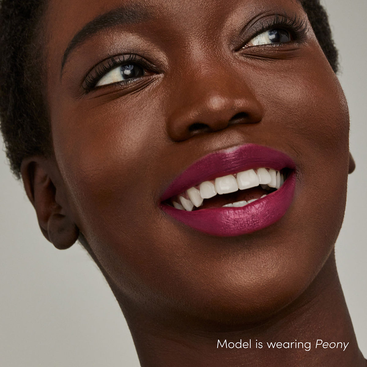 A smiling person wearing Jane Iredale ColorLuxe Hydrating Cream Lipstick in a deep berry shade with a bold satin finish.