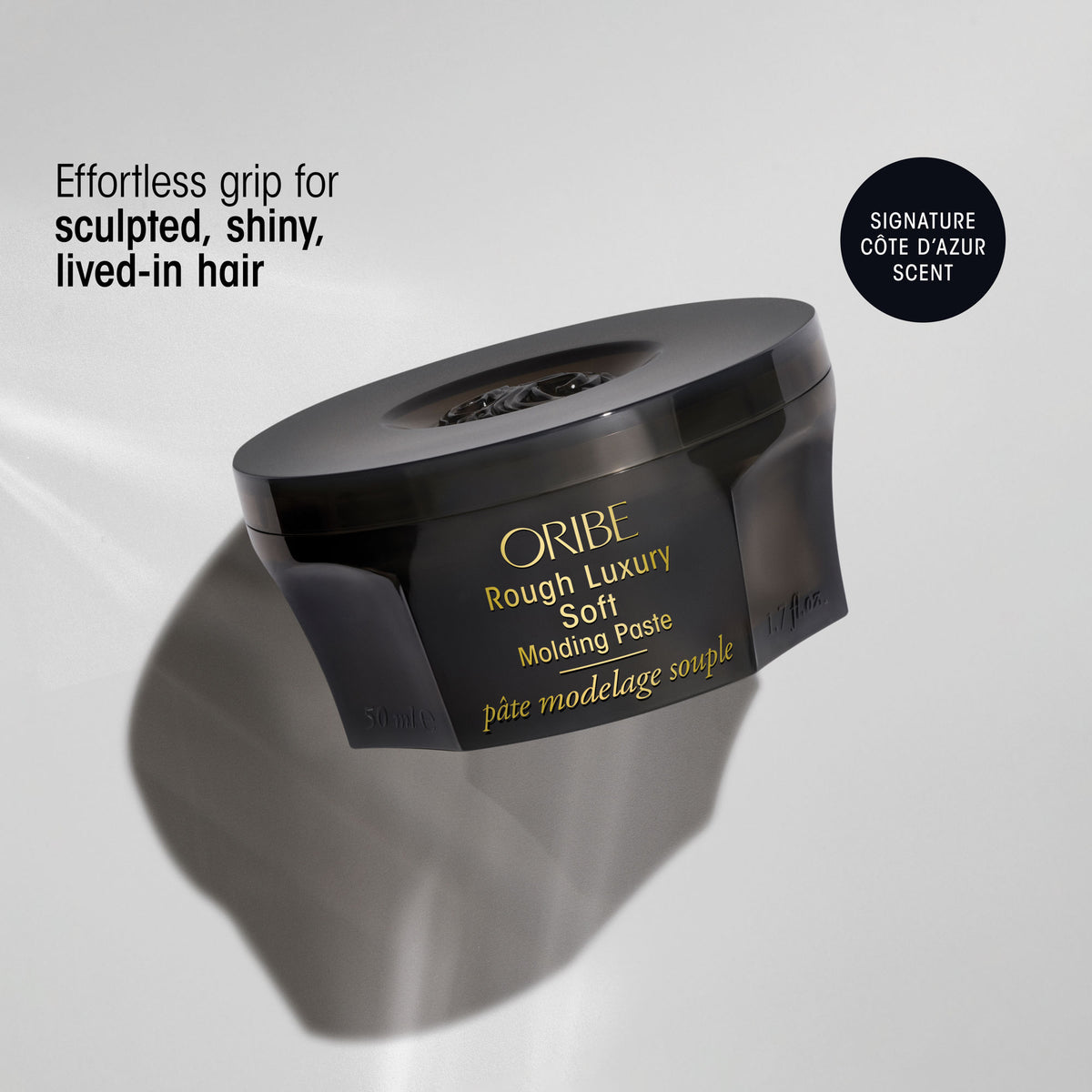 A jar of Oribe Rough Luxury Soft Molding Paste for Definition & Shine featuring text that reads Effortless grip for sculpted, shiny, lived-in hair and a badge noting Signature Côte dAzur Scent.