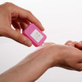 Hands holding a small, rectangular pink bottle of Ellis Brooklyn Florist Eau de Parfum and applying a drop to a wrist.