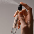 A hand presses the nozzle of a small glass Radio Bombay Eau de Parfum bottle, releasing a fine mist amidst the heat of Bandra.