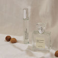 A cylindrical rollerball and a square glass bottle of Maison Louis Marie No.04 Bois de Balincourt Eau de Parfum rest on draped fabric next to three whole nutmegs, evoking fresh forests and the smell after rain.
