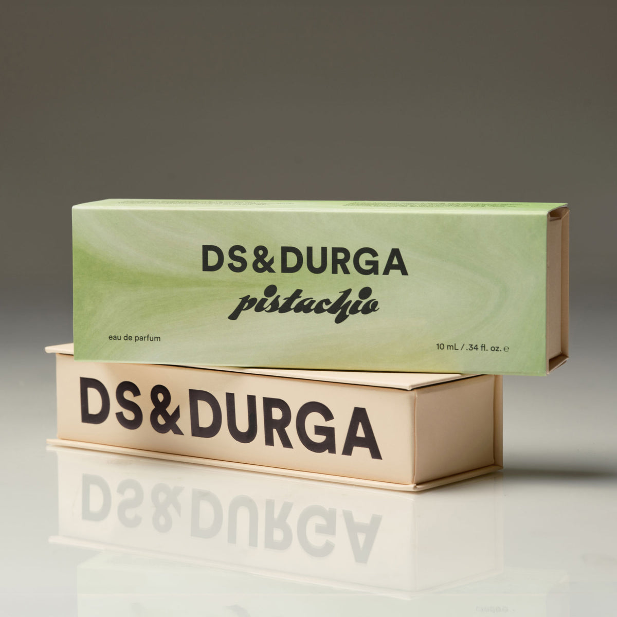 Two rectangular boxes of D.S. & Durga Pistachio Eau de Parfum stacked on a reflective surface, with the light green pistachio box on top and the cream-colored box showing brand text on the bottom.