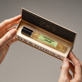 Hands holding an open box containing a small pistachio D.S. & Durga Pistachio Eau de Parfum glass rollerball bottle with a light green label.