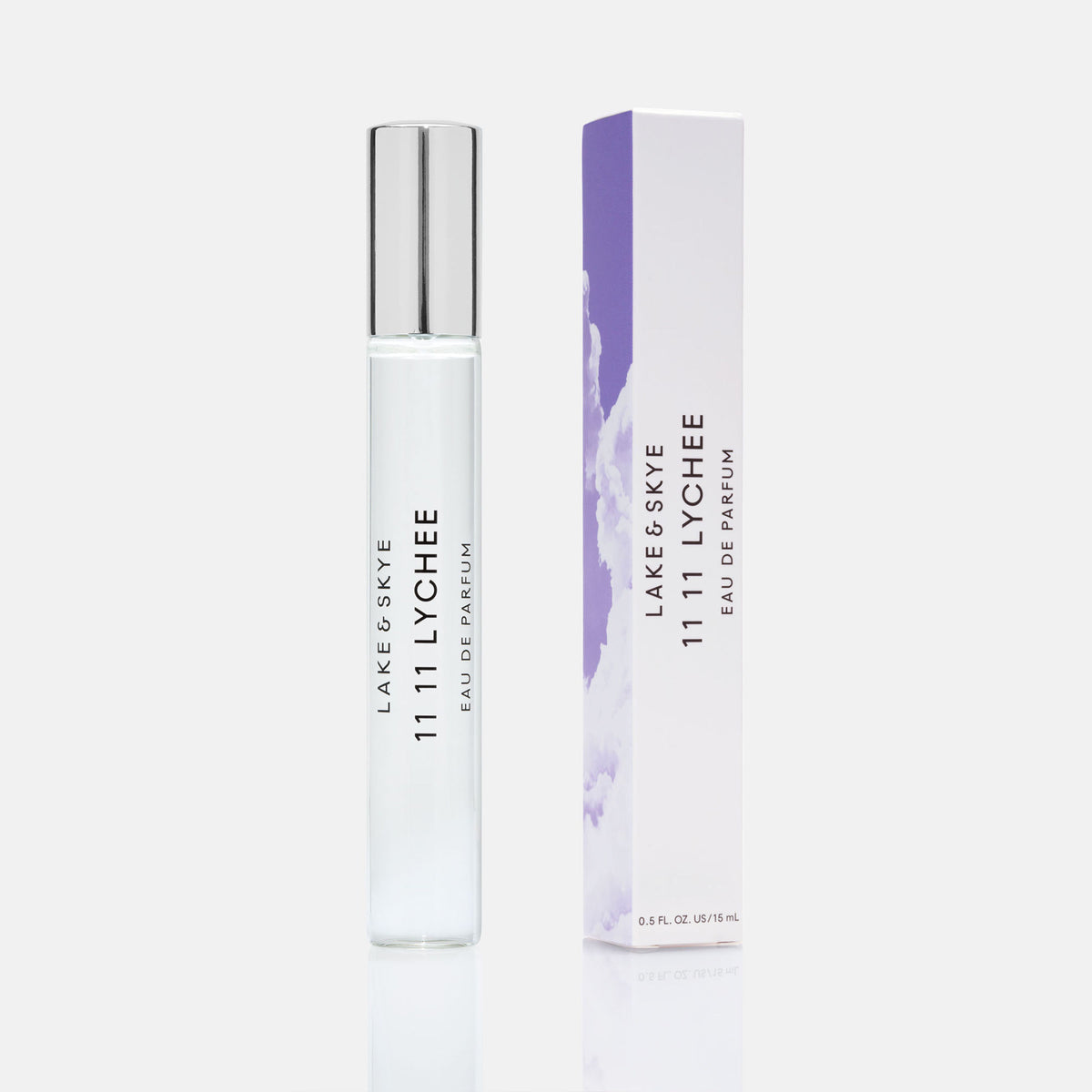 A slim glass rollerball of 11 11 Lychee Eau de Parfum by Lake & Skye next to its tall, purple-accented box featuring a cloud pattern.