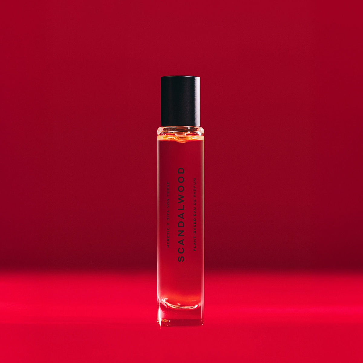 A cylindrical glass rollerball of Heretic Scandalwood Eau de Parfum with a black cap, featuring the scent name on the label.