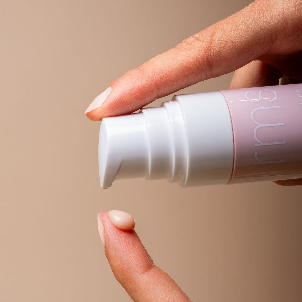 A finger catches a small drop of pale pink RMS Beauty ReEvolve Radiance Locking Primer dispensed from a refillable pump bottle.