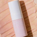 A cylindrical refillable pump bottle of RMS Beauty ReEvolve Radiance Locking Primer resting on a smear of light-colored gel.