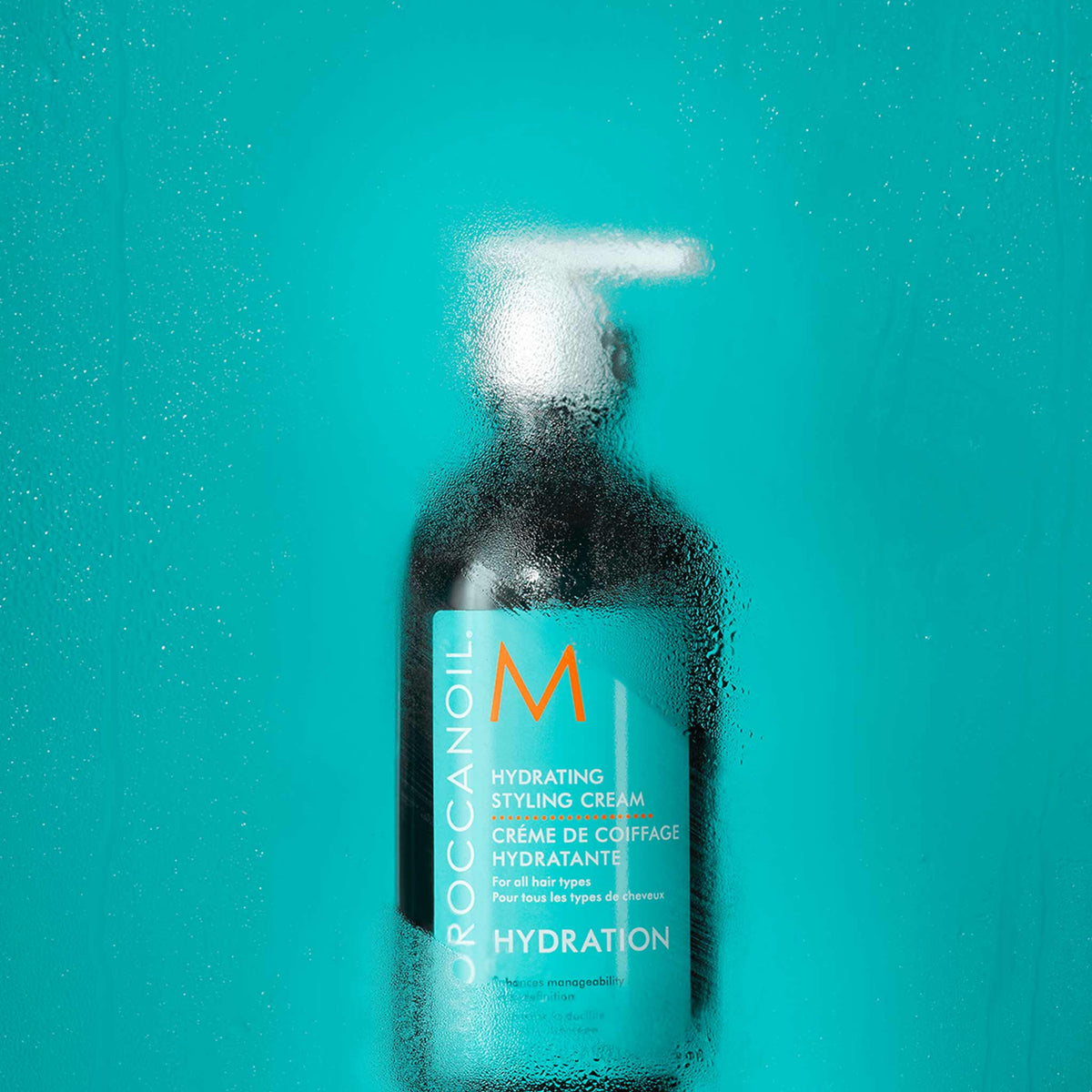 A bottle of Moroccanoil Hydrating Styling Cream for smoothing fly-aways sits behind a condensation-covered surface.