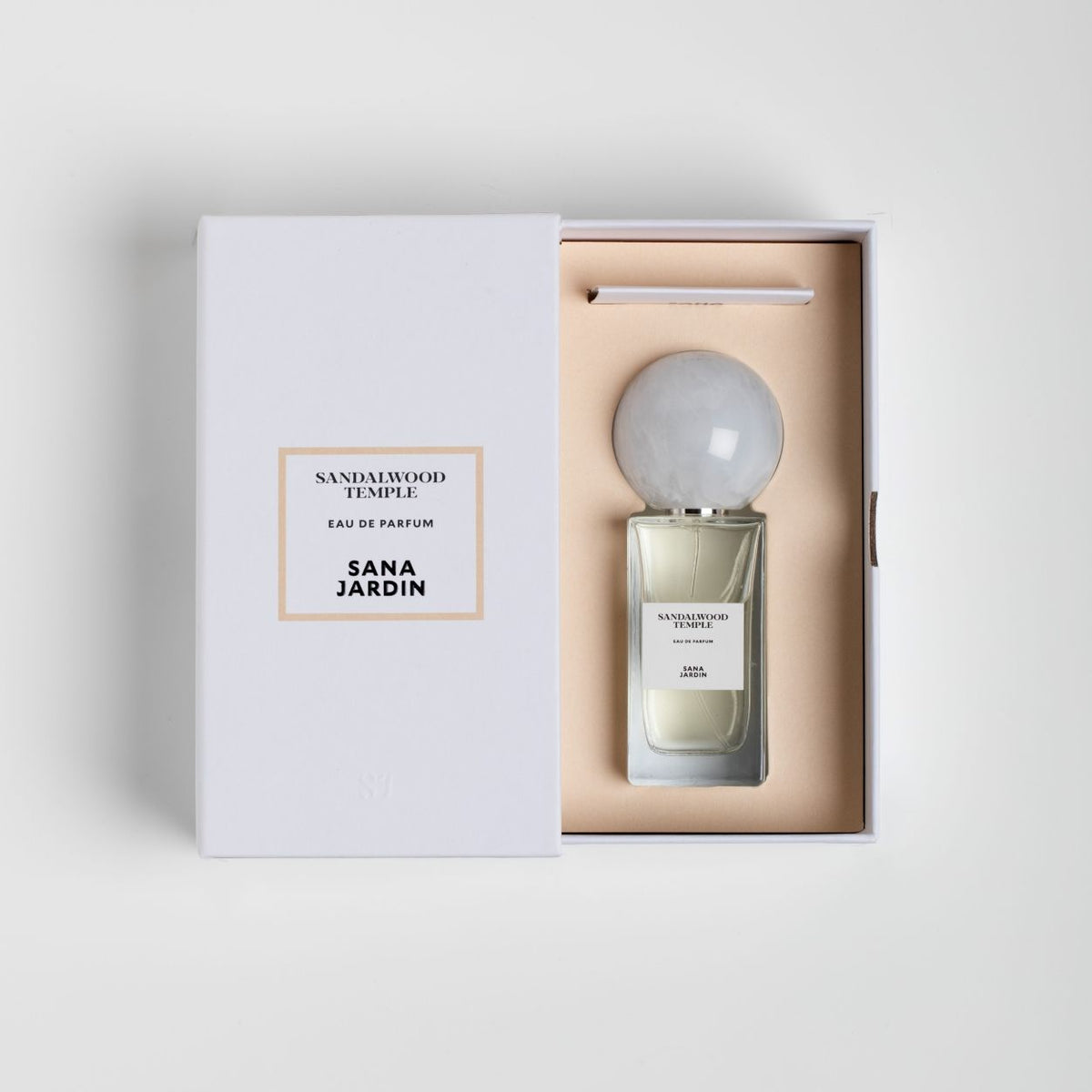 A rectangular Sana Jardin Sandalwood Temple Eau de Parfum bottle with a large, round grey cap sits inside an open white gift box, with the product name and brand printed on the box cover and the bottle label.