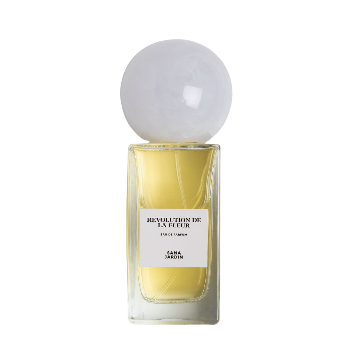 A rectangular glass bottle of Sana Jardin Revolution De La Fleur Eau de Parfum, filled with yellow liquid, topped with a large, spherical white cap and a label reading Eau de Parfum.