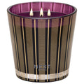 A three-wick Nest New York Autumn Plum Candle in a deep purple glass vessel decorated with vertical black and gold stripes.