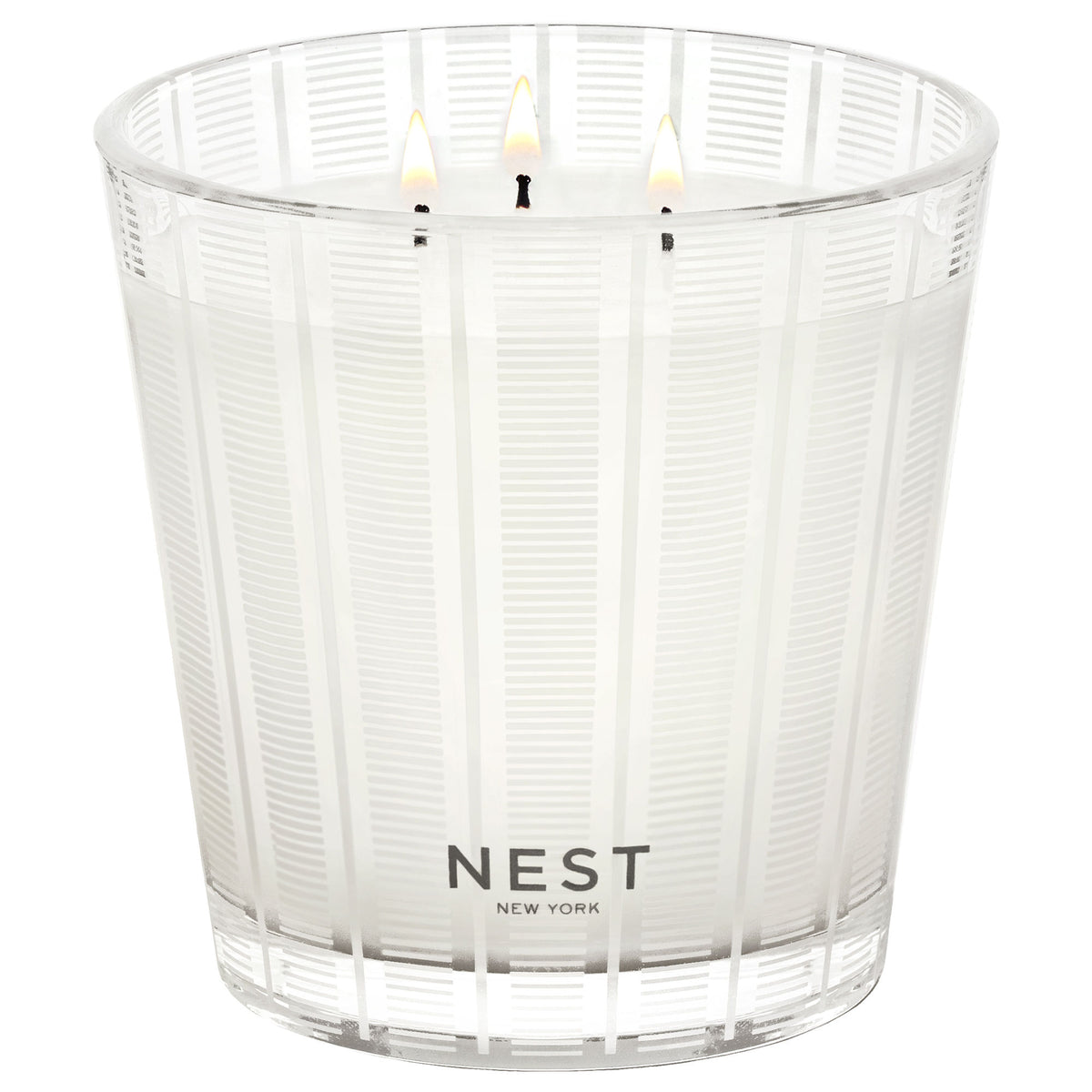 A Nest New York Moroccan Amber three-wick candle in a clear glass vessel with a white striped pattern and a burning flame, creating an exotic atmosphere.