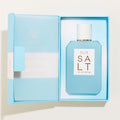 A rectangular bottle of Ellis Brooklyn Salt Eau de Parfum in light blue with a white cap, housed in an open light blue gift box that evokes salty skin and tropical florals.