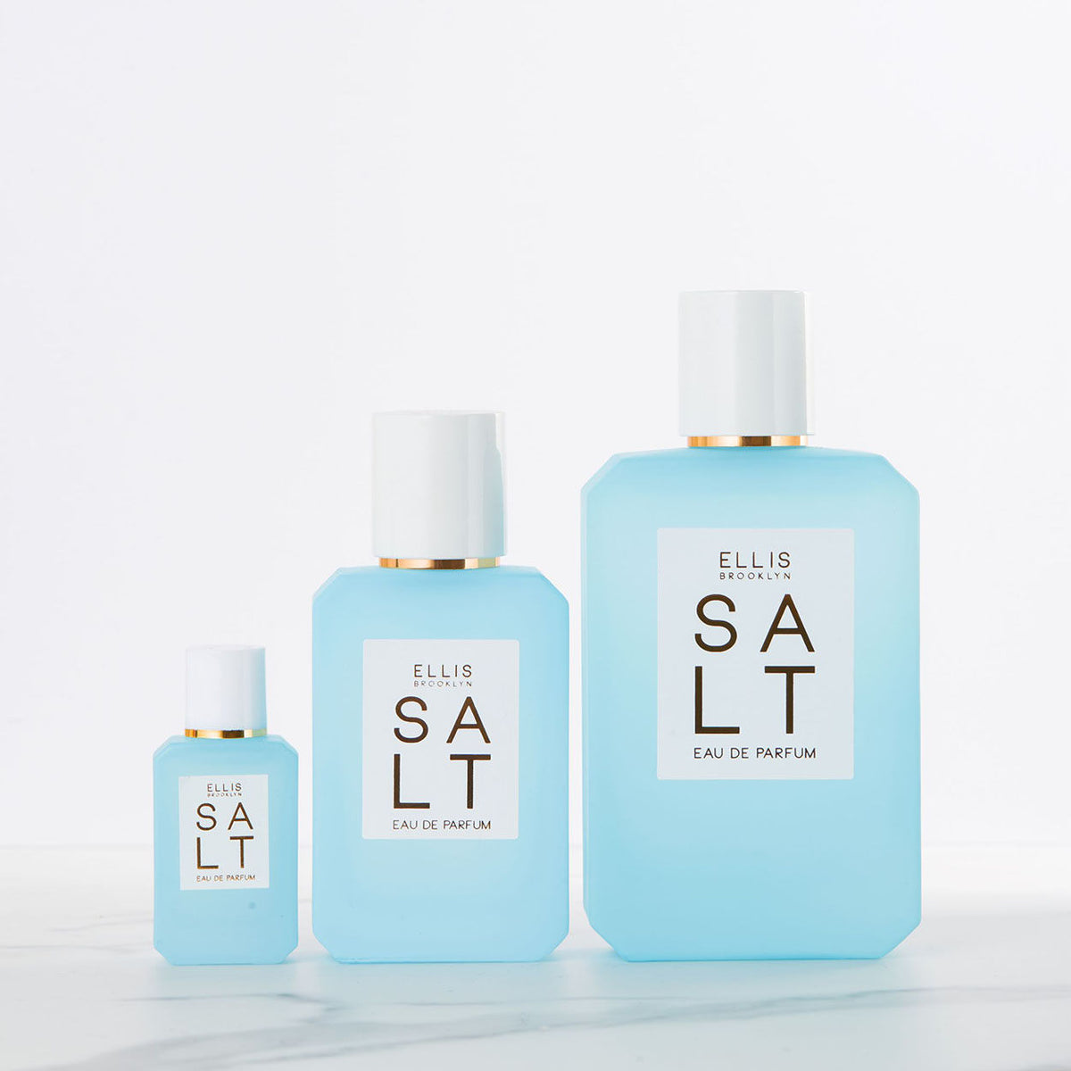 Three bottles of Ellis Brooklyn Salt Eau de Parfum in varying sizes, each with a white cap and a label evoking salty skin and tropical florals.