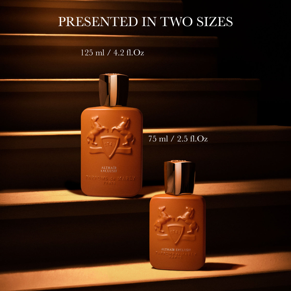 Two amber-colored Althaïr Exclusif Parfum bottles of 125 ml and 75 ml, featuring notes of saffron and Bourbon vanilla, resting on steps.