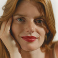 A close-up portrait of a woman with red hair wearing intense Phyto-Rouge Shine lipstick and resting her chin on her hand.