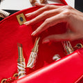 A hand reaches into a red handbag containing two gold and white zebra-print Phyto-Rouge Shine lipsticks that offer an intense color payoff.