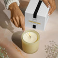 Hands lighting a glass jar of Lafco Chamomile Lavender candle next to its boxed packaging.