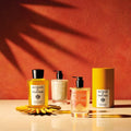 Two Buongiorno Eau de Parfum bottles, a bottle of lotion, and a cylindrical box evoking spring in Tuscany arranged on a surface against a terracotta-colored wall.